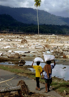 A woman and her son carry bags as they walk amid the destruction in sumatra