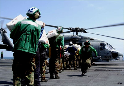 U.S. Navy personnel load bags of rice on a helicopter