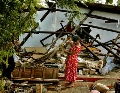 A woman holds her baby as she stands in her destroyed home in Sri Lanka